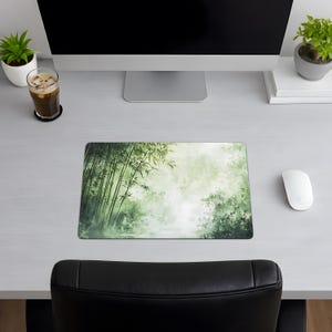 Desk mat with a green bamboo forest design, placed on a light wood desk with a computer, tablet, and blue hydrangea flowers in a gray pot.