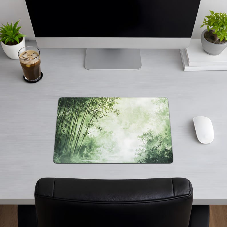 Desk mat with a green bamboo forest design, placed on a light wood desk with a computer, tablet, and blue hydrangea flowers in a gray pot.