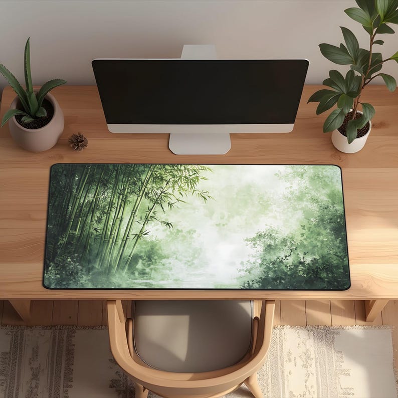 Desk mat with a green bamboo forest design, placed on a light wood desk with a computer, tablet, and blue hydrangea flowers in a gray pot.