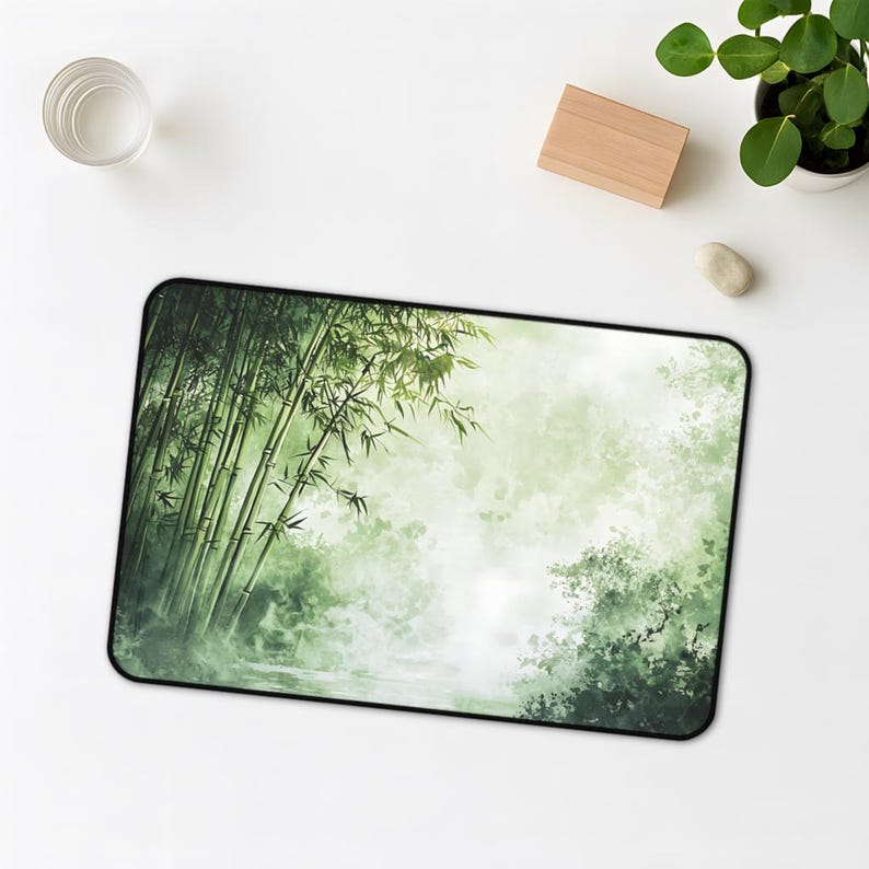 Desk mat with a green bamboo forest design, placed on a light wood desk with a computer, tablet, and blue hydrangea flowers in a gray pot.