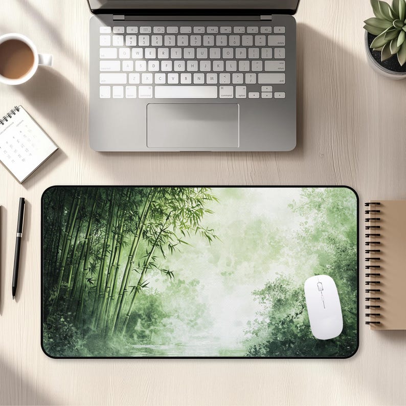 Desk mat with a green bamboo forest design, placed on a light wood desk with a computer, tablet, and blue hydrangea flowers in a gray pot.