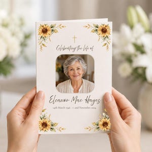 May include: A funeral programme booklet with a white background, featuring watercolour sunflowers in the corners, a gold cross, and a central photo of an older person. The text reads: Celebrating the life of Eleanor Mae Hayes, 14th March 1946 – 2nd November 2024.