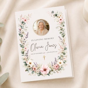 Op de afbeelding: Een herdenkingskaart met een foto van een vrouw, omringd door een bloemenkrans van roze, witte en groene bloemen. De tekst luidt "In Loving Memory Olivia Jones" met data eronder. Een witte kaars is zichtbaar.