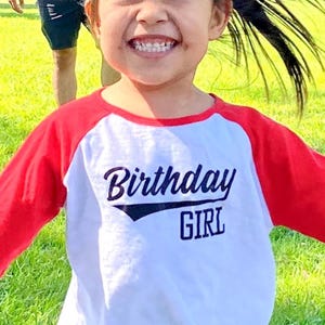 Può includere: Una maglietta bianca e rossa in stile raglan con la scritta "Birthday GIRL" in blu navy. La maglietta ha maniche rosse e un corpo bianco, perfetta per una festa di compleanno.