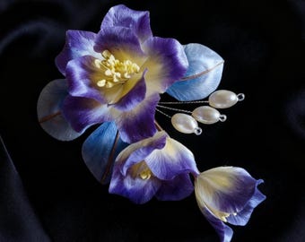 Könnte beinhalten: Handgefertigtes Haaraccessoire mit Stoffblumen in Lila und Gelb, mit blauen Akzenten und Perlen. Die Blütenblätter haben ein zartes, geschichtetes Aussehen. Der Schmuck ist vor einem schwarzen Hintergrund platziert.