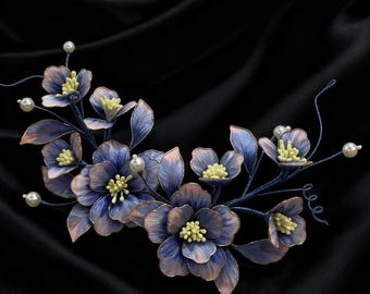 May include: A delicate floral hair piece with blue and pink flowers, yellow centres, and pearl embellishments. The flowers are arranged on a dark blue wire frame. The background is a black satin fabric, creating a luxurious look.