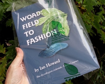 May include: A blue book with the title "WOAD: FIELD TO FASHION" and the text "by Ian Howard" and "Blue dye with green credentials: A farmer's journey". The book is wrapped in a clear plastic bag with a green label that says "100% DEGRADABLE" and "www.epl-global.com epl."