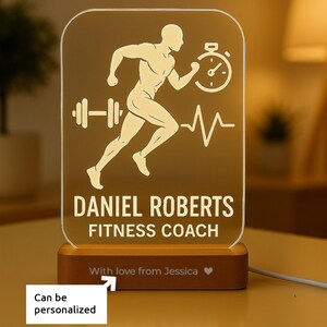 May include: A personalized fitness coach lamp with a running figure, stopwatch, and heartbeat line design. The lamp includes the name "DANIEL ROBERTS" and the title "FITNESS COACH". The base is wooden, and the text "With love from Jessica" is included.