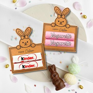 Può includere: Set regalo a tema pasquale con due cartelli di cartone sormontati da coniglietti dei cartoni animati. Un cartello contiene due barrette di cioccolato Kinder, l'altro due barrette Yogurette. Sono presenti anche un coniglietto di cioccolato e uova di Pasqua decorate.