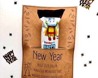 May include: A New Year's gift presentation featuring a Kinder Happy Hippo candy bar. The candy is in a brown paper pocket with the words "New Year" and a German message. Black star and confetti decorations are scattered around the gift.