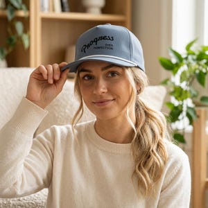 May include: A light blue baseball cap featuring a white cord trim along the brim and the black text Progress OVER PERFECTION printed on the front. The cap has a structured crown and a curved visor, providing a clean and simple design aesthetic.