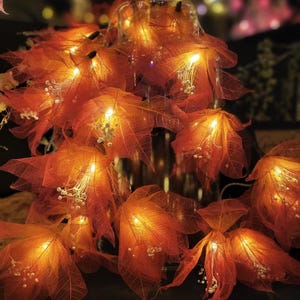 May include: Orange leaf string lights with small white accents and warm white LED lights. The leaves are arranged around a glass container, creating a cozy, autumnal ambiance. Perfect for fall decor or special events.