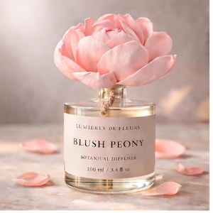 May include: A clear glass botanical diffuser with a large, light pink peony flower on top. The label reads "Blush Peony, Botanical Diffuser, 100 ml / 3.4 fl oz". Several pink petals are scattered around the base of the bottle.