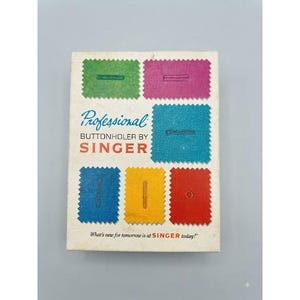 May include: A rectangular white box for a Professional Buttonholer by Singer. The front features colorful fabric swatches in green, pink, blue, yellow, and red, each with a stitched buttonhole. Text includes Professional, BUTTONHOLER BY SINGER.