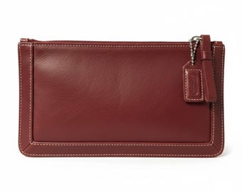 Cartera de mano Coach de piel color burdeos con cremallera, neceser de cosméticos, estilo vintage clásico.
