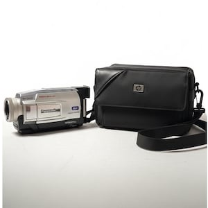 May include: A silver and black Panasonic camcorder with a black carrying case. The camcorder has a lens on the front and the words "Panasonic" and "700x Digital Zoom" printed on the side. The black carrying case has a shoulder strap and the HP logo.