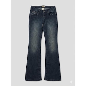 May include: Dark wash denim jeans with a slight flare at the bottom. The jeans have a classic five-pocket design, a button and zipper closure, and small rhinestone accents near the front pockets. The brand name "Mudd" is visible on the label.