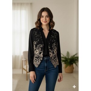 以下が含まれることがあります： 精巧な金色の花の刺繍が施された黒いベスト。黒いブラウスの上に着用し、ブルージーンズと組み合わせています。明るい部屋で、ニュートラルな背景でスタイリングされています。