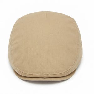 May include: A solid beige flat cap featuring a rounded crown and a short, stiff brim. The hat is constructed from a durable, woven fabric with visible stitching along the edges and seams, presenting a clean, structured, and classic silhouette.