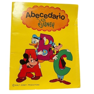 May include: A vintage children's book with a bright yellow cover. The title "Abecedario Disney" is displayed in a decorative orange bubble. Mickey Mouse, Donald Duck, and Goofy are featured with the letters A, B, and C. The book is a Walt Disney Production.