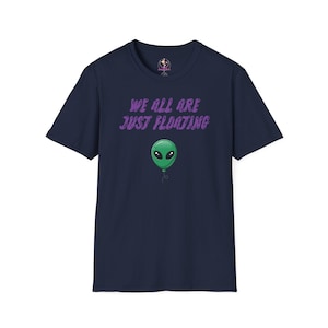 Peut inclure: Un t-shirt bleu marine à manches courtes avec le texte violet "WE ALL ARE JUST FLOATING" imprimé au-dessus d'un graphique représentant une tête d'extraterrestre verte en forme de ballon avec une fine ficelle noire suspendue en dessous.