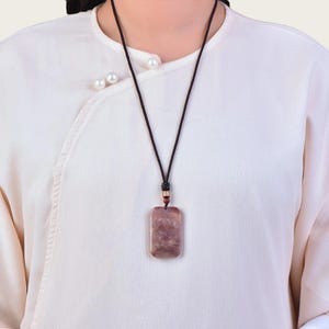May include: A brown and white stone pendant on a black cord necklace. The pendant is rectangular and has a marbled pattern.