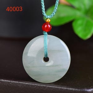 May include: A jade pendant necklace with a circular, light green stone. The pendant is suspended from a teal cord, accented with a red bead and a gold-colored bead. The number "40003" is in the upper left corner.