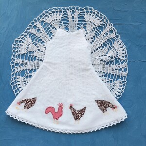 May include: White crocheted doily with a white towel sewn to the centre. The towel has a pink and brown embroidered design of three chickens.