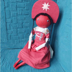 May include: A handmade doll with a red dress, white sleeves, and a red hat with a white star. The doll has black hair and a red face.