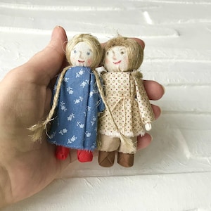 May include: Two handmade fabric dolls, one with a blue and white floral dress and red shoes, the other with a beige and brown floral dress and brown shoes.