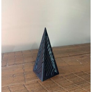 May include: A black pyramid-shaped ornament with a wavy pattern on all sides.