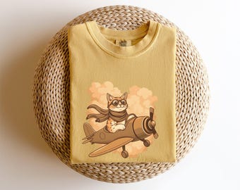 May include: A yellow t-shirt with a cartoon cat wearing aviator goggles and flying a vintage airplane. The cat is wearing a scarf and the airplane is flying through clouds. The t-shirt has the text "Little Tales" on the tag.