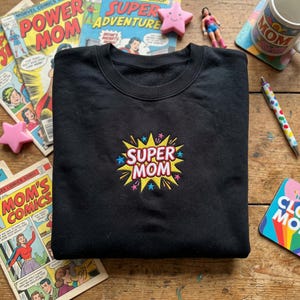 May include: A white ceramic mug with a black handle and the text "But First, Coffee" in a black, bold font. The mug is on a white surface.