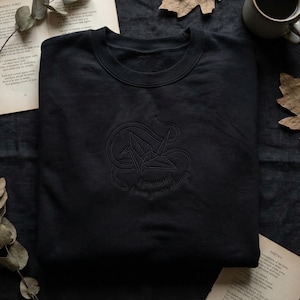 May include: Black crewneck sweatshirt with an embroidered origami crane design. The design includes the words "promised I was yours always" in a cursive font. The sweatshirt is made of a soft material.