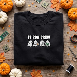 May include: A black crewneck sweatshirt featuring a white embroidered graphic of four ghosts with the text IT BOO CREW. The first ghost wears a headset, the second uses a laptop, the third holds a wrench, and the fourth holds a circuit board.