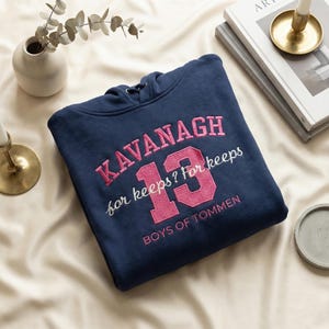 May include: Navy blue hoodie with the name "KAVANAGH" embroidered in pink, along with the number "13" and the phrase "for keeps? For keeps". The text "BOYS OF TOMMEN" is also embroidered on the hoodie.