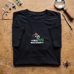 May include: A black short-sleeved t-shirt featuring an embroidered graphic of a black spider wearing a brown detective hat and holding a magnifying glass. The text BUG is in green and the text BUG BOUNTY is in white below the spider graphic.
