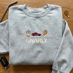 May include: A heather gray sweatshirt with embroidered graphics of a bubble tea, a red sports car, and a fried chicken leg. The word "GNARLY" is embroidered below the graphics.