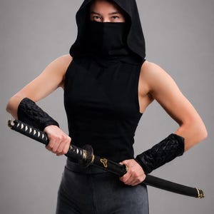 Peut inclure: Un haut noir sans manches à capuche avec un masque assorti, associé à des protège-bras noirs matelassés et un short gris foncé. La tenue est accessoirisée avec un katana noir doté d'accents dorés sur la garde et le fourreau.