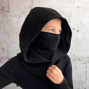Könnte beinhalten: Ein schwarzer Kapuzen-Schal mit Gesichtsbedeckung. Der Schal ist aus weichem, warmem Stoff gefertigt und perfekt, um Kopf und Hals bei kaltem Wetter warm zu halten.