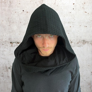 May include: A person wearing a black hooded sweatshirt with a textured fabric. The hood is pulled up over their head, and their eyes are visible.