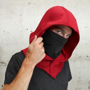 K&ouml;nnte beinhalten: Eine Person tr&auml;gt ein rotes Kleidungsst&uuml;ck mit Kapuze und einer schwarzen Gesichtsbedeckung. Die Kapuze ist &uuml;ber den Kopf gezogen, und die Gesichtsbedeckung ist &uuml;ber Nase und Mund gezogen.