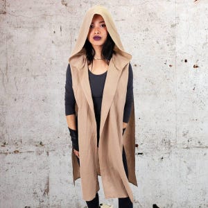 May include: A long, tan hooded vest with a shawl collar. The vest is made of a soft, lightweight fabric and has a relaxed fit.