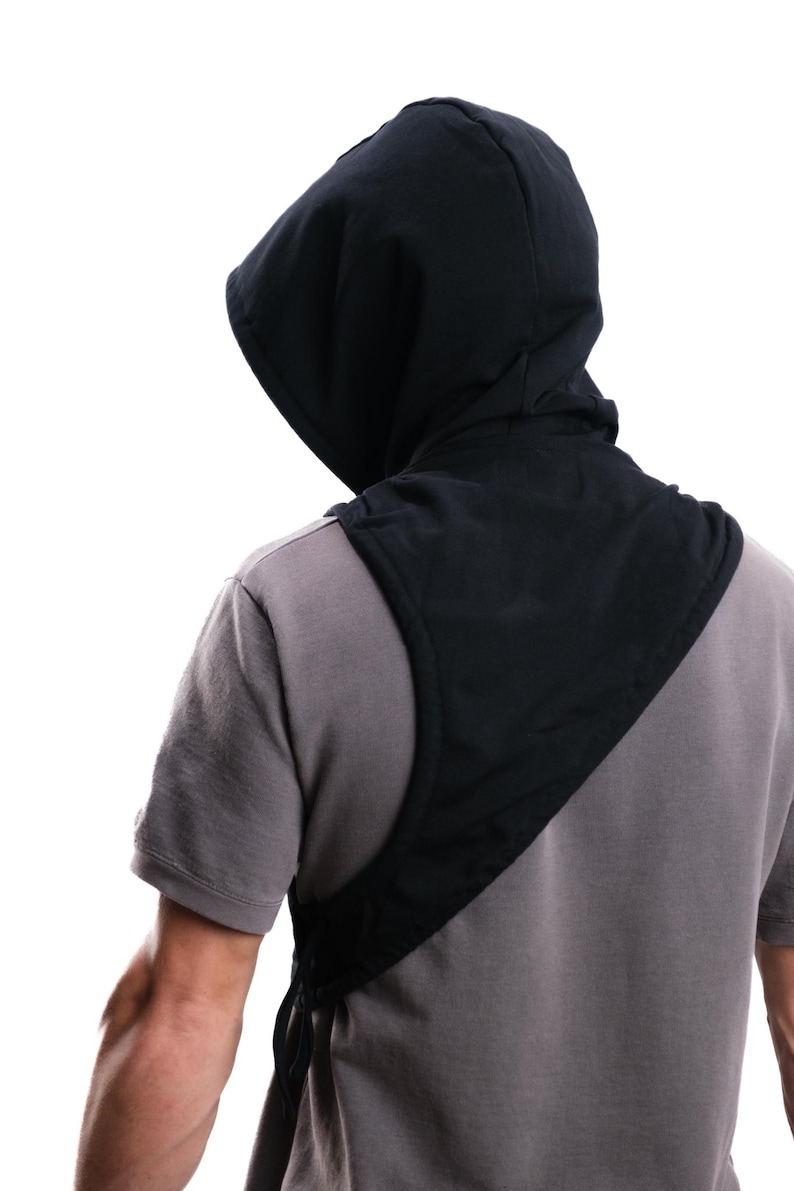 Op de afbeelding: Zwarte nekwarmer met capuchon, ontworpen om over de schouders te worden gedragen. De capuchon is bevestigd aan een slab-achtig stuk dat zich over de borst en rug uitstrekt. De nekwarmer is gemaakt van een gladde, donkere stof.