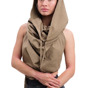 May include: A tan-colored hooded top with a halter neckline and drawstring detail. The top is made of a soft fabric and is worn with dark gray shorts. The hood drapes around the neck and shoulders.
