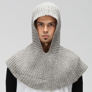 May include: A light gray knitted hood with a textured, ribbed pattern that covers the head and drapes over the shoulders. The garment features a wide opening around the face and a thick, woven construction, providing full coverage for the head and neck.
