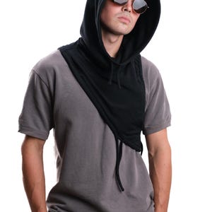Op de afbeelding: Een zwarte sjaal met capuchon en trekkoord, gedragen over een grijs t-shirt. De sjaal is over de schouders gedrapeerd. De persoon draagt ​​ronde zonnebrillen.
