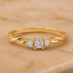 Op de afbeelding: Een gouden ring met een gedraaid bandontwerp en drie heldere, rond geslepen stenen in het midden. De middelste steen is iets groter dan de twee stenen ernaast, allemaal vastgehouden door kleine gouden pootjes op een gepolijste gouden ring.