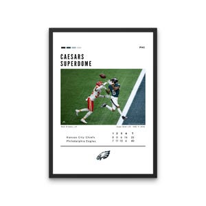 May include: Framed print featuring a football game scene with players in action. The text "CAESARS SUPERDOME" is at the top, with game scores and team names below. The Philadelphia Eagles logo is at the bottom.