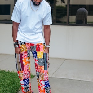 May include: A plain white short-sleeved t-shirt paired with loose-fitting trousers featuring a vibrant patchwork design. The pants are composed of various rectangular fabric segments in red, yellow, blue, and white, showcasing diverse geometric and floral patterns.